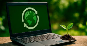 Ordenador portátil con un símbolo de reciclaje sobre el planeta Tierra en la pantalla y una pequeña planta creciendo al lado, representando la sostenibilidad y la economía circular en PC Renova.
