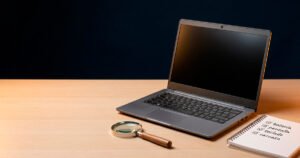 Portátil usado sobre un escritorio, con una lupa y una libreta, representando la evaluación de su estado antes de venderlo